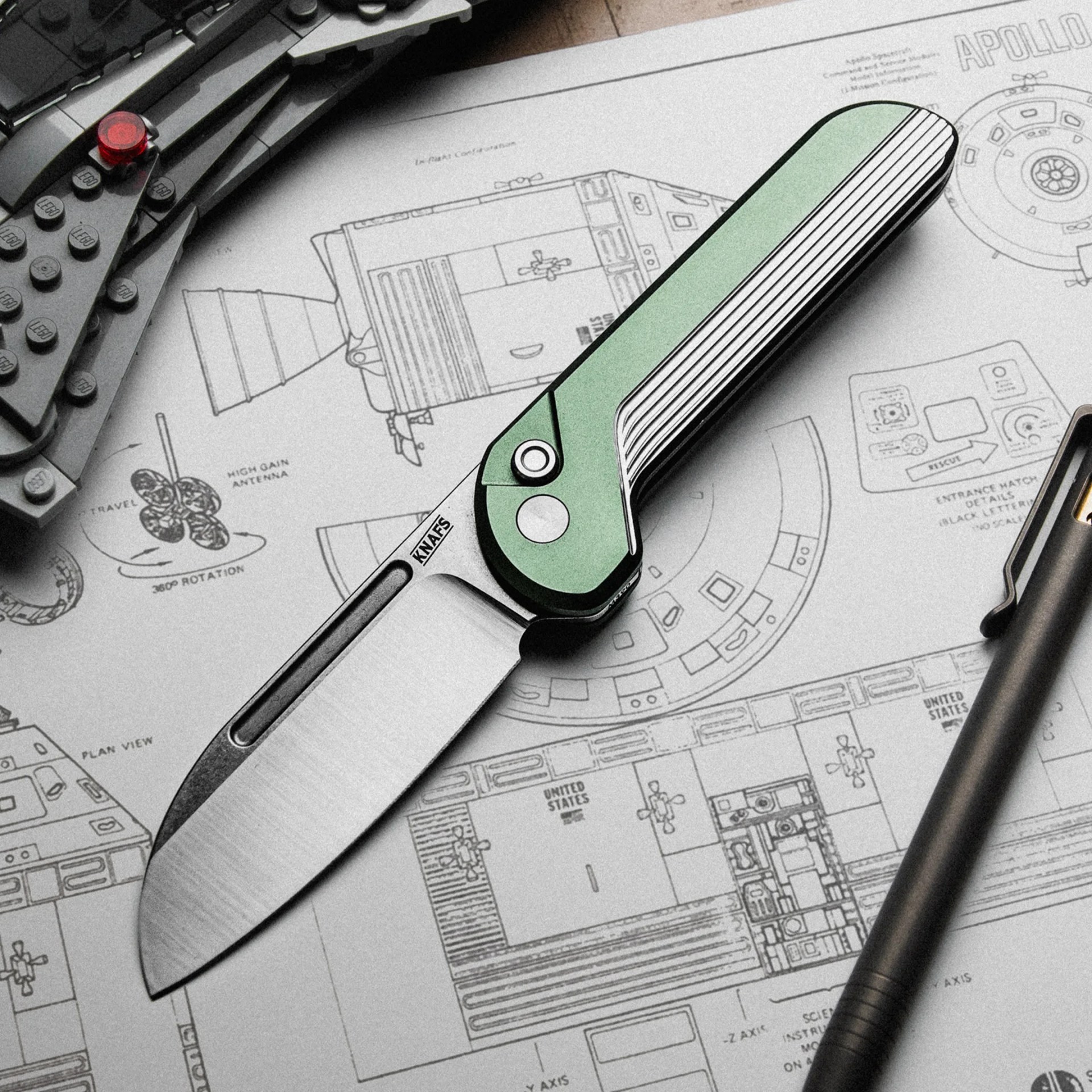 Green and black folding knife with a partially serrated stainless steel blade on a blueprint.