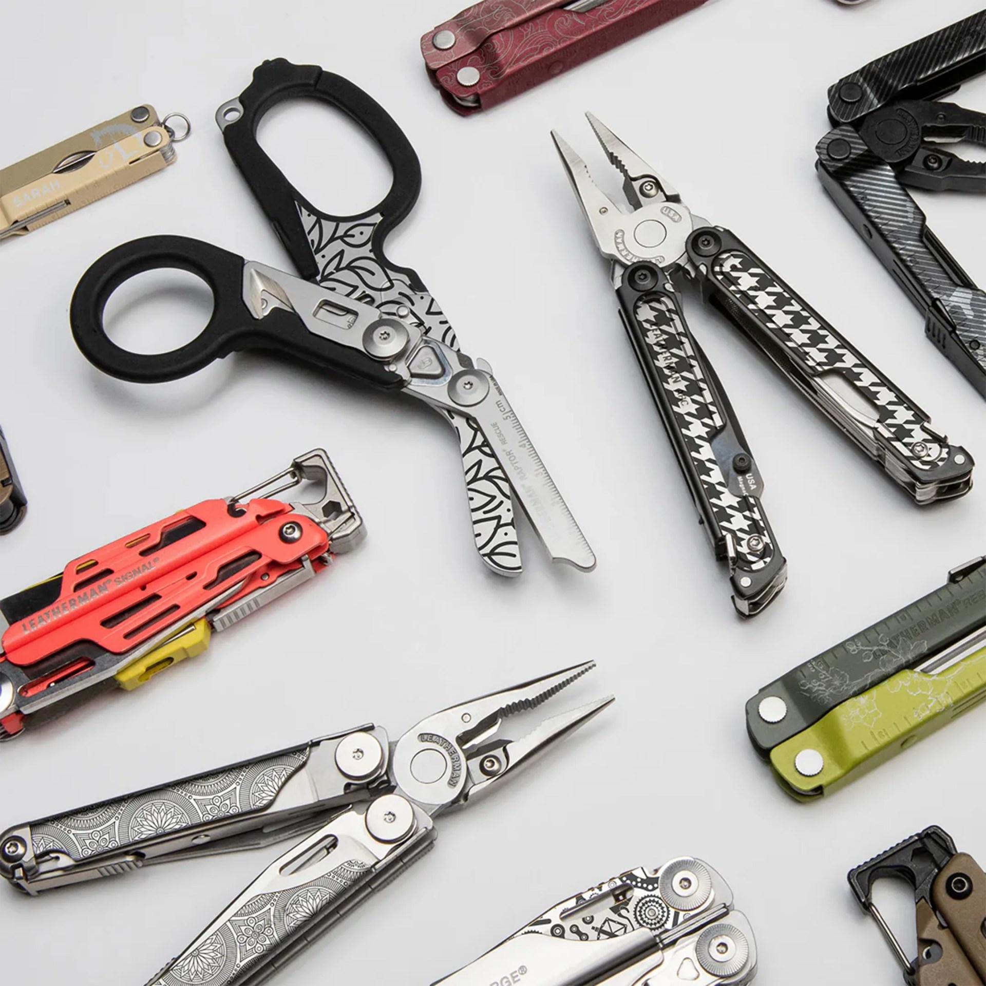Collection of multi-tool pliers and scissors with various patterned handles on a white surface.