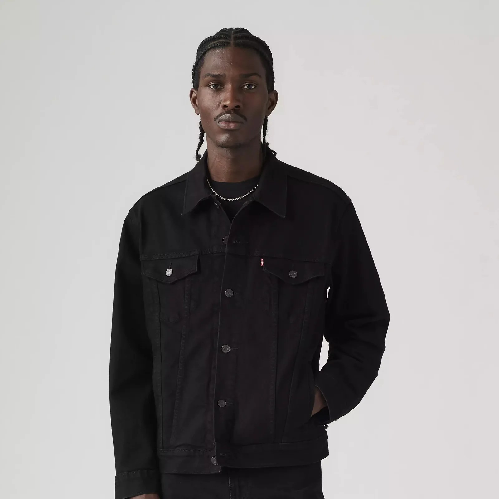 Black denim jacket with button closures and chest pockets worn by a person against a plain light background.