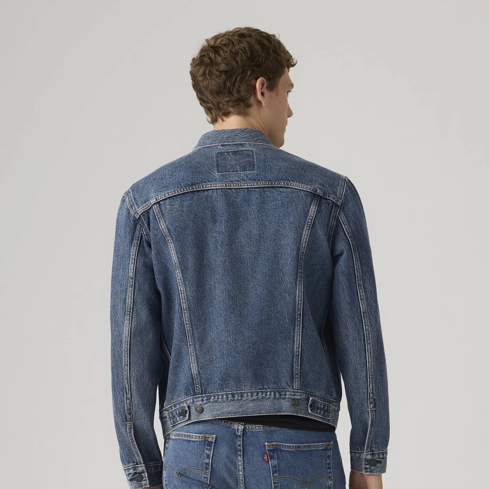 Back view of a person wearing a blue denim jacket and matching blue denim jeans.