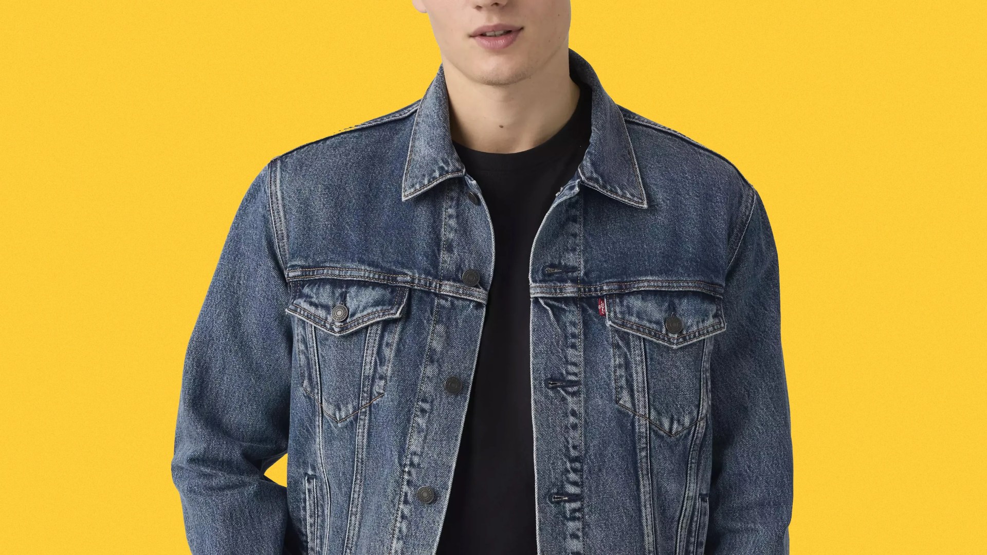 Blue denim jacket with buttoned chest pockets worn over a black shirt against a yellow background.