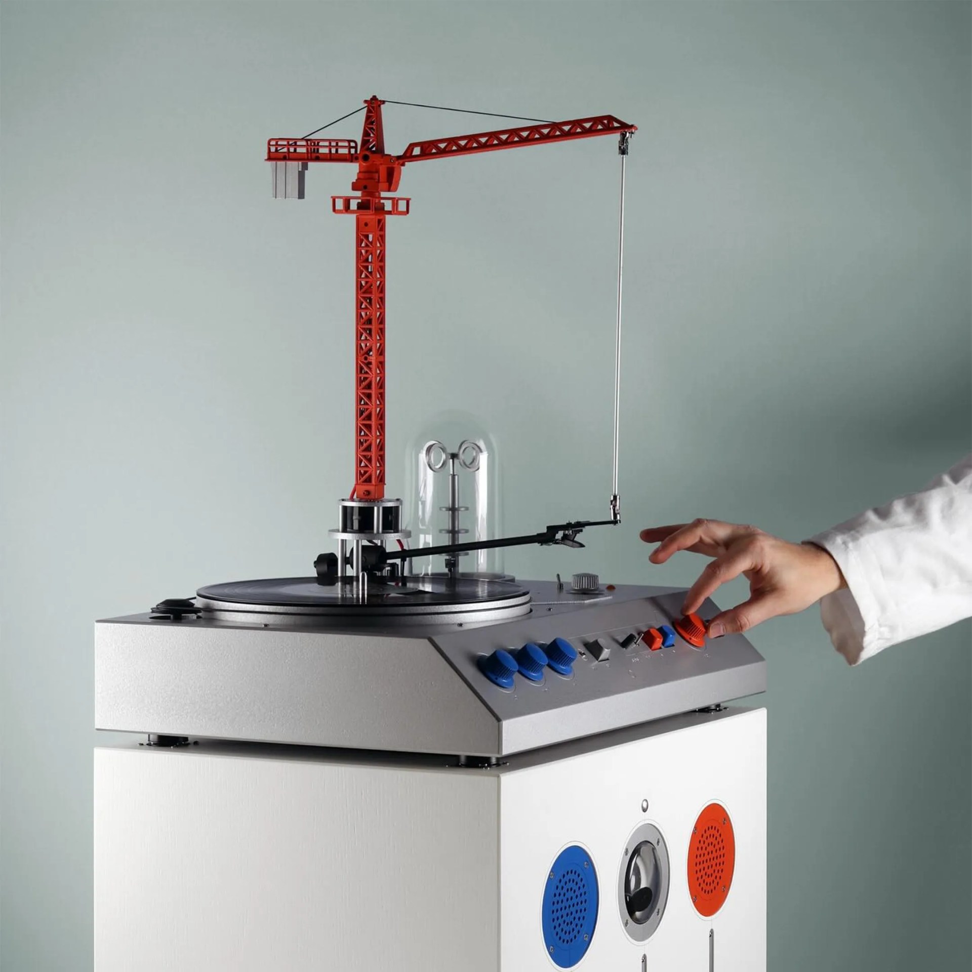 Turntable with a red crane-shaped tonearm and control knobs in blue and orange on a white base.