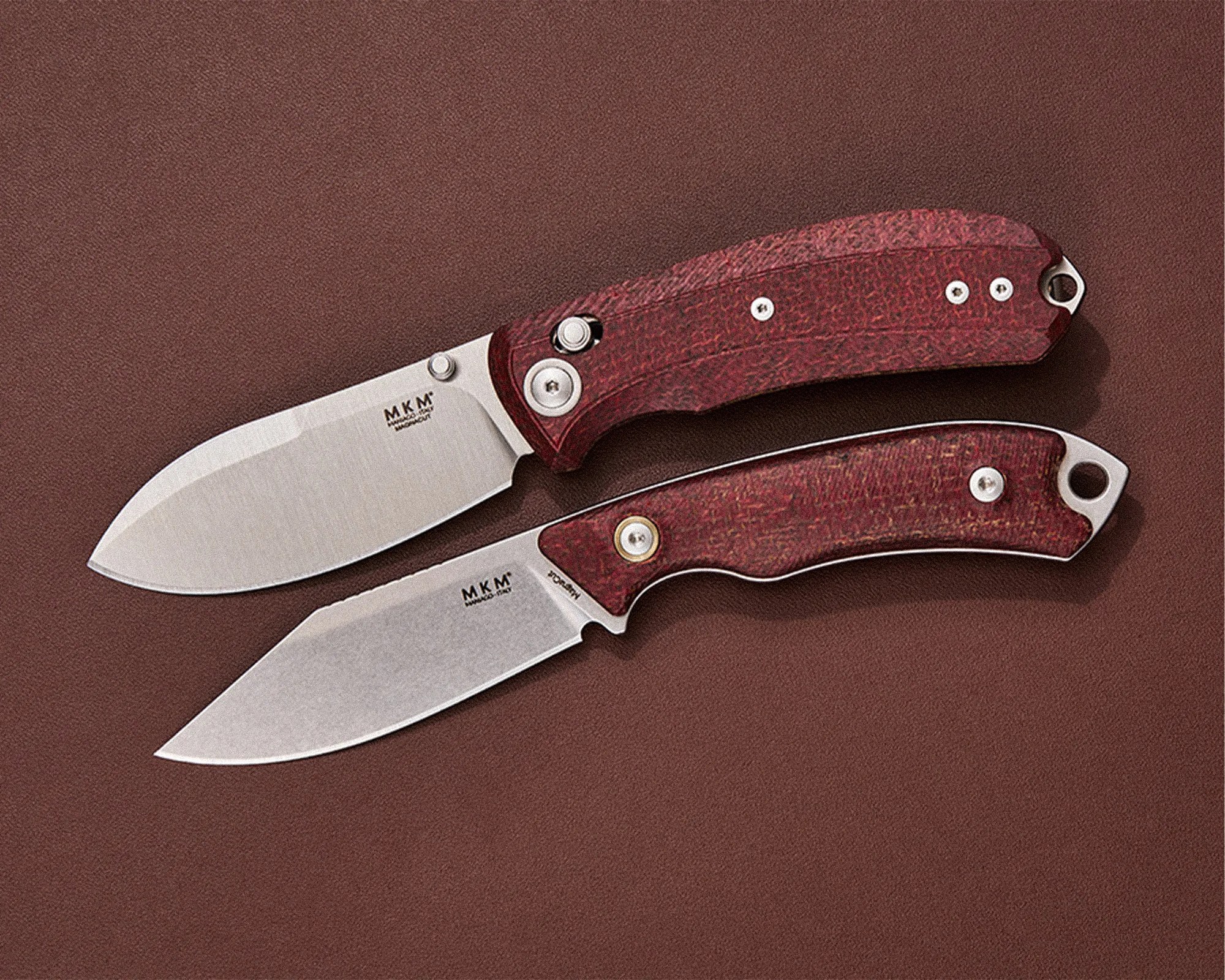 Two folding knives with red textured handles and stainless steel blades on a brown surface.