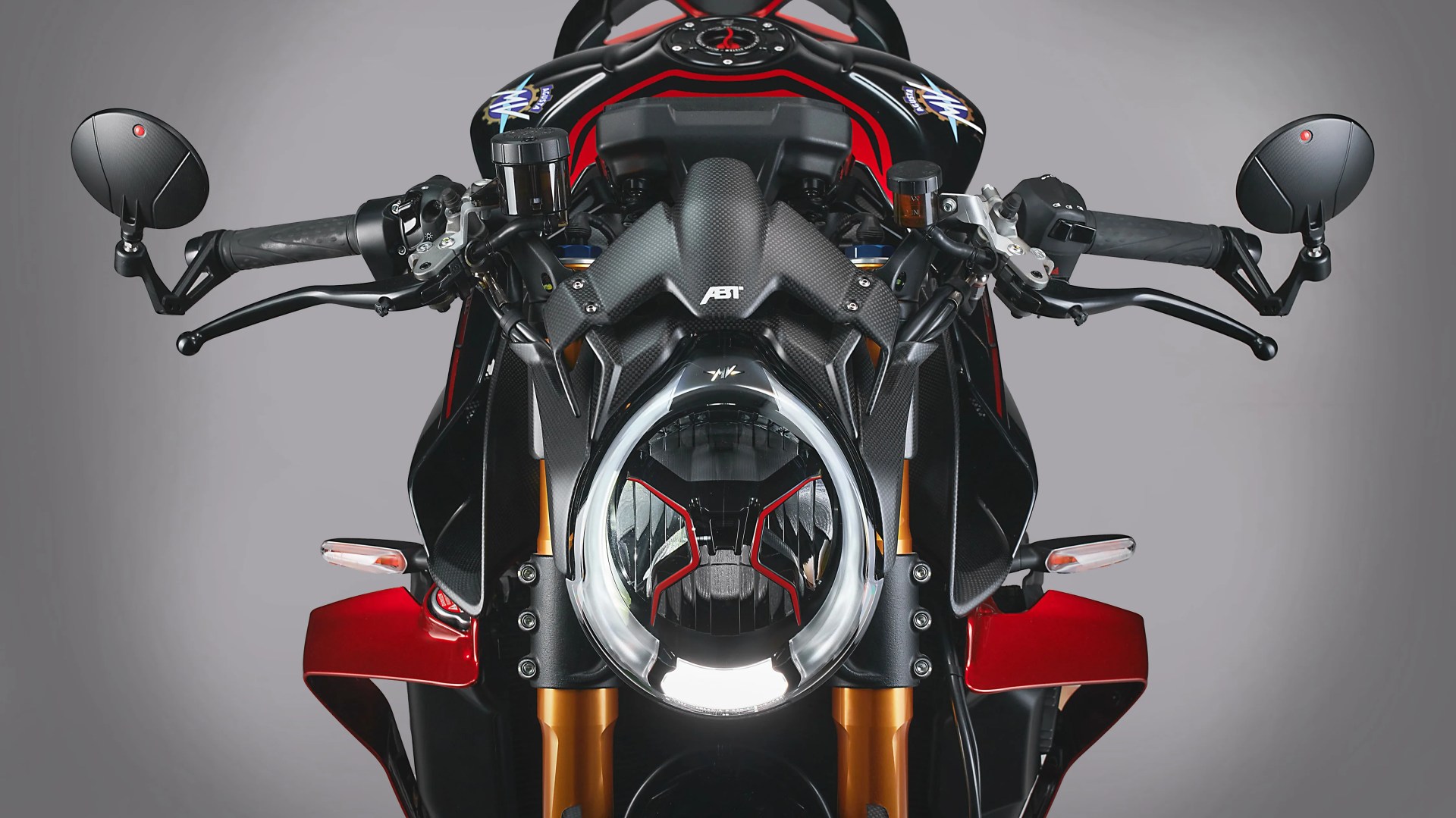 Close-up of a motorcycle front with carbon fiber fairing, round headlight, black handlebars, and red accents.