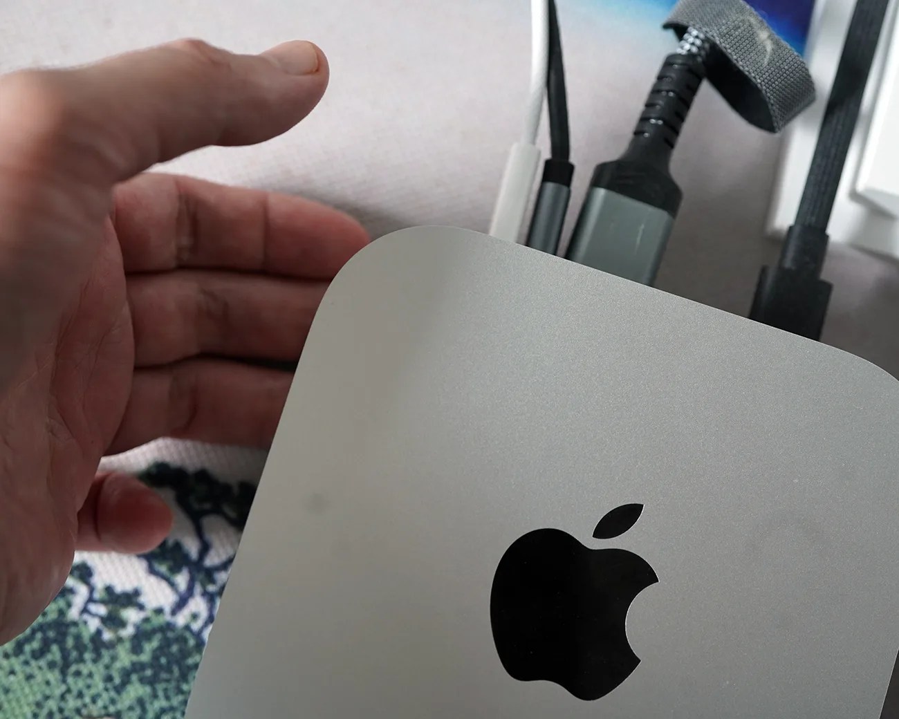 Silver Apple Mac Mini with black Apple logo and multiple cables connected, next to a hand.