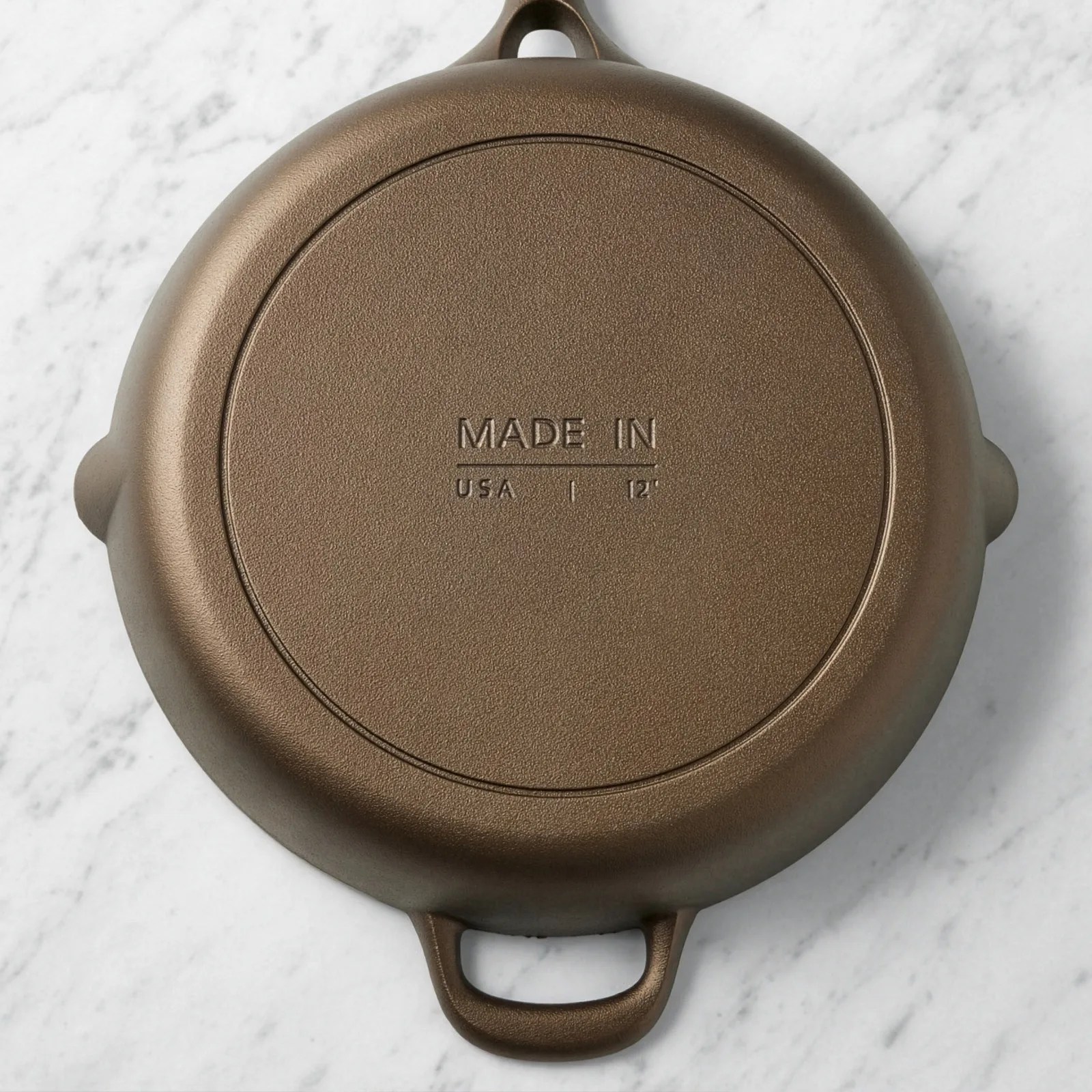 Bottom of a brown cast iron skillet with "Made in USA 12"" embossed on it, on a white marble surface.