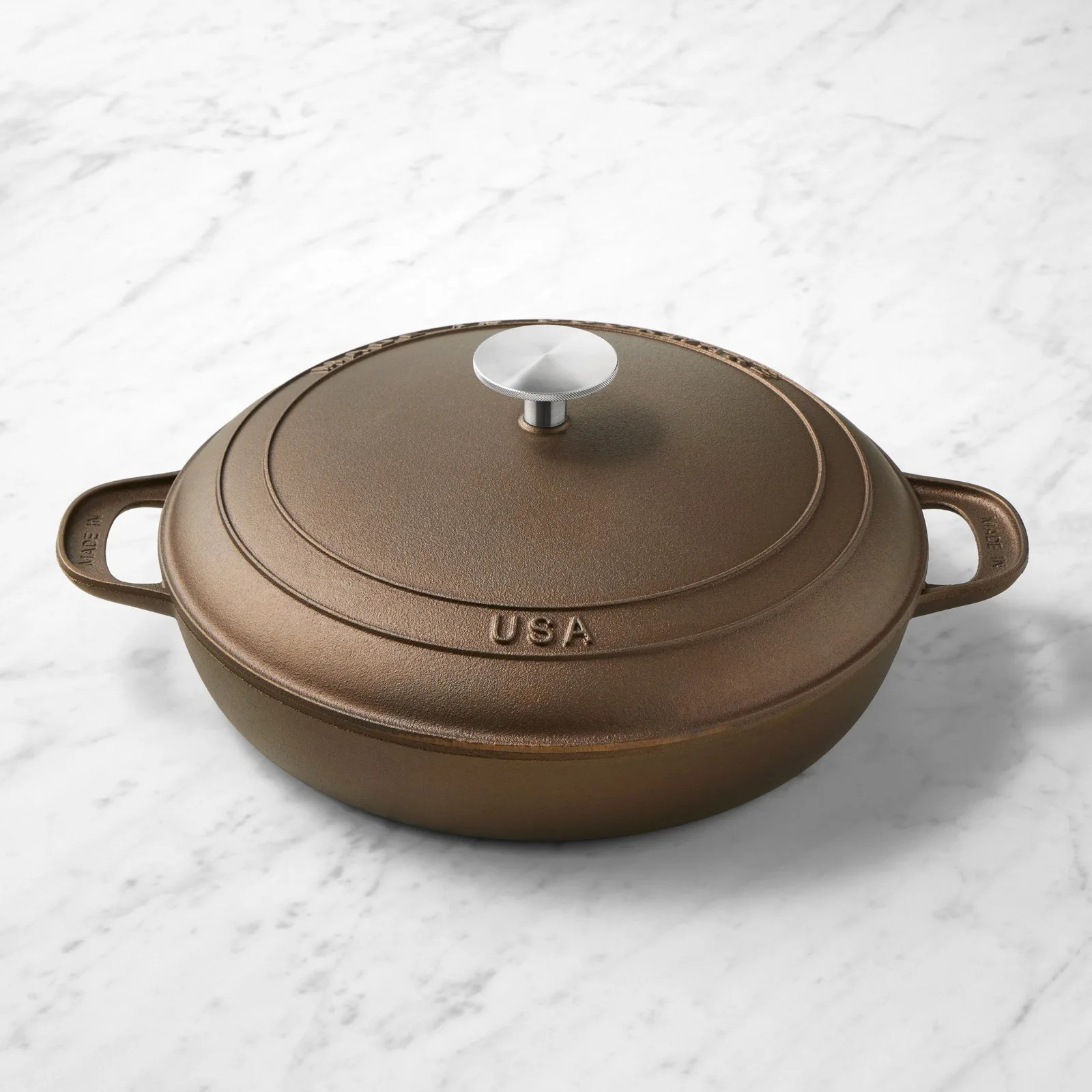 Brown cast iron Dutch oven with lid and metal knob on a white marble surface.