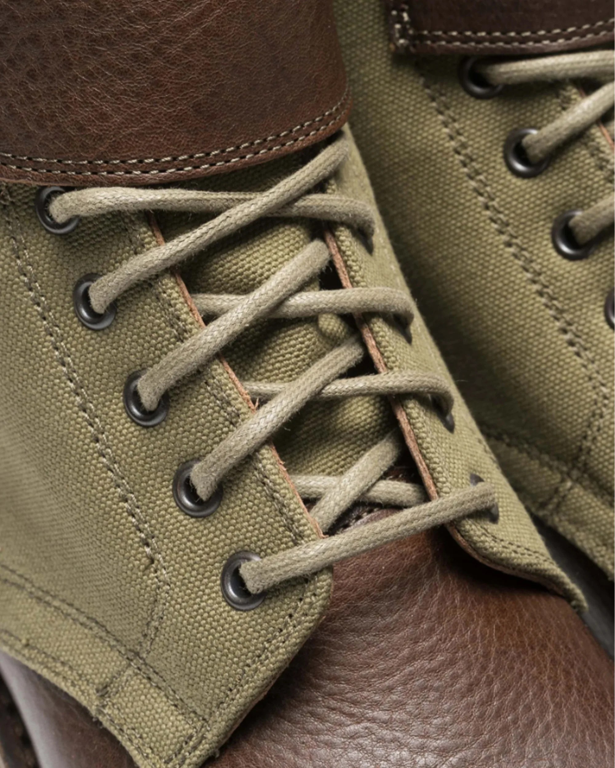 Close-up of olive green canvas and brown leather boot with beige laces threaded through black metal eyelets.