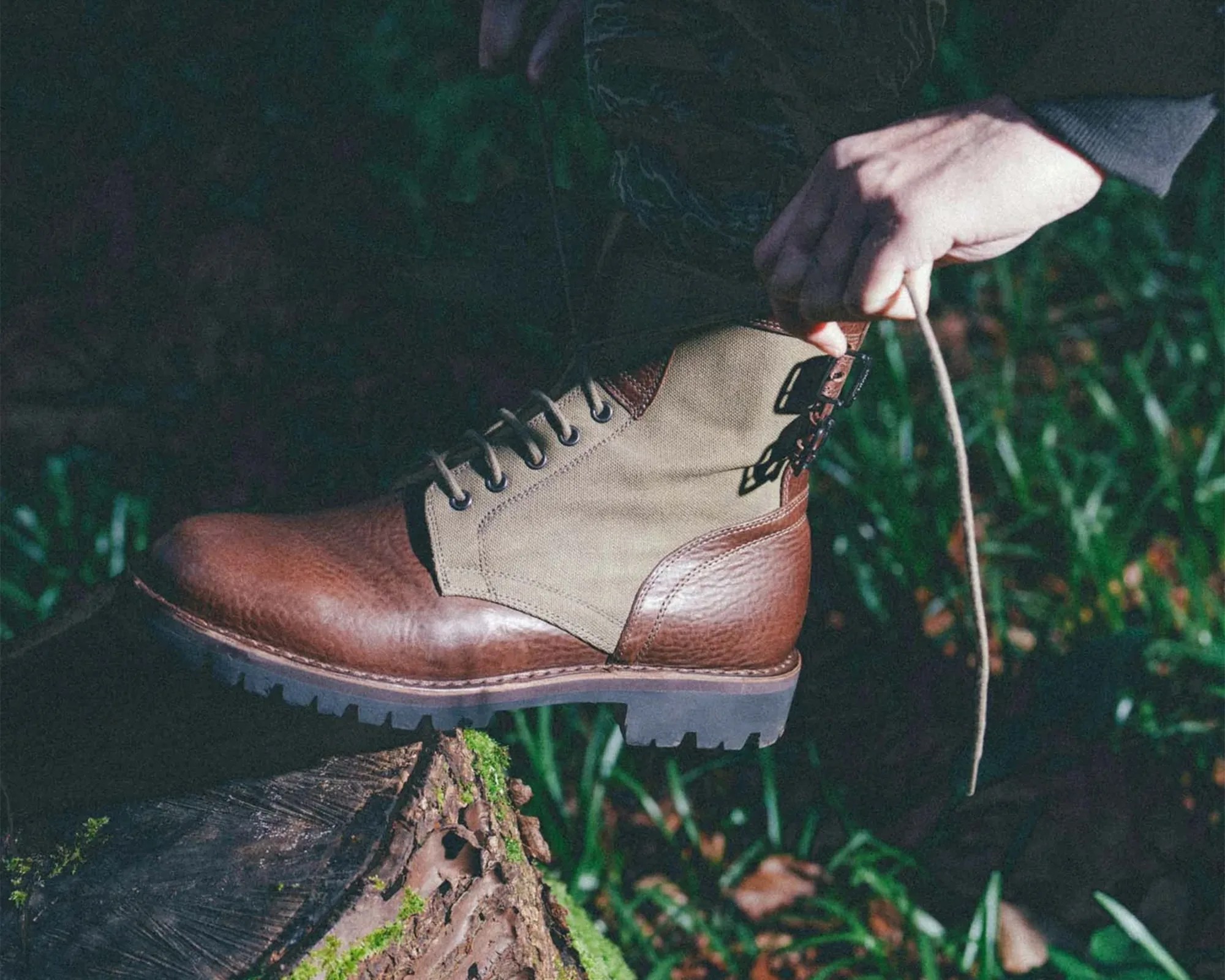 Brown and beige leather and fabric hiking boot with laces and buckle being tied on a tree stump.