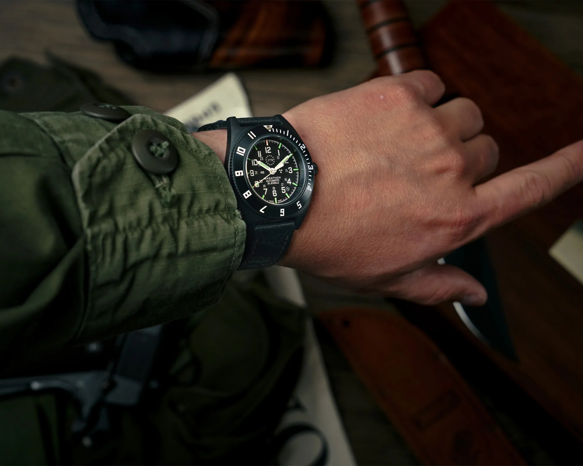 Black Marathon automatic wristwatch with white numerals and green accents on a wrist wearing a green jacket.