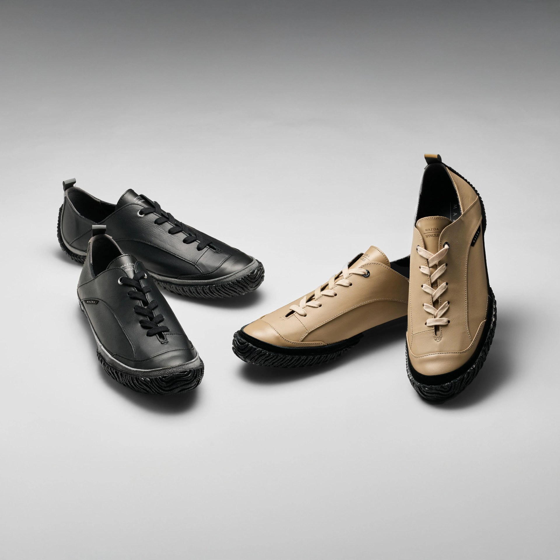 Two pairs of leather lace-up shoes, one black and one beige, with textured black soles on a gray surface.