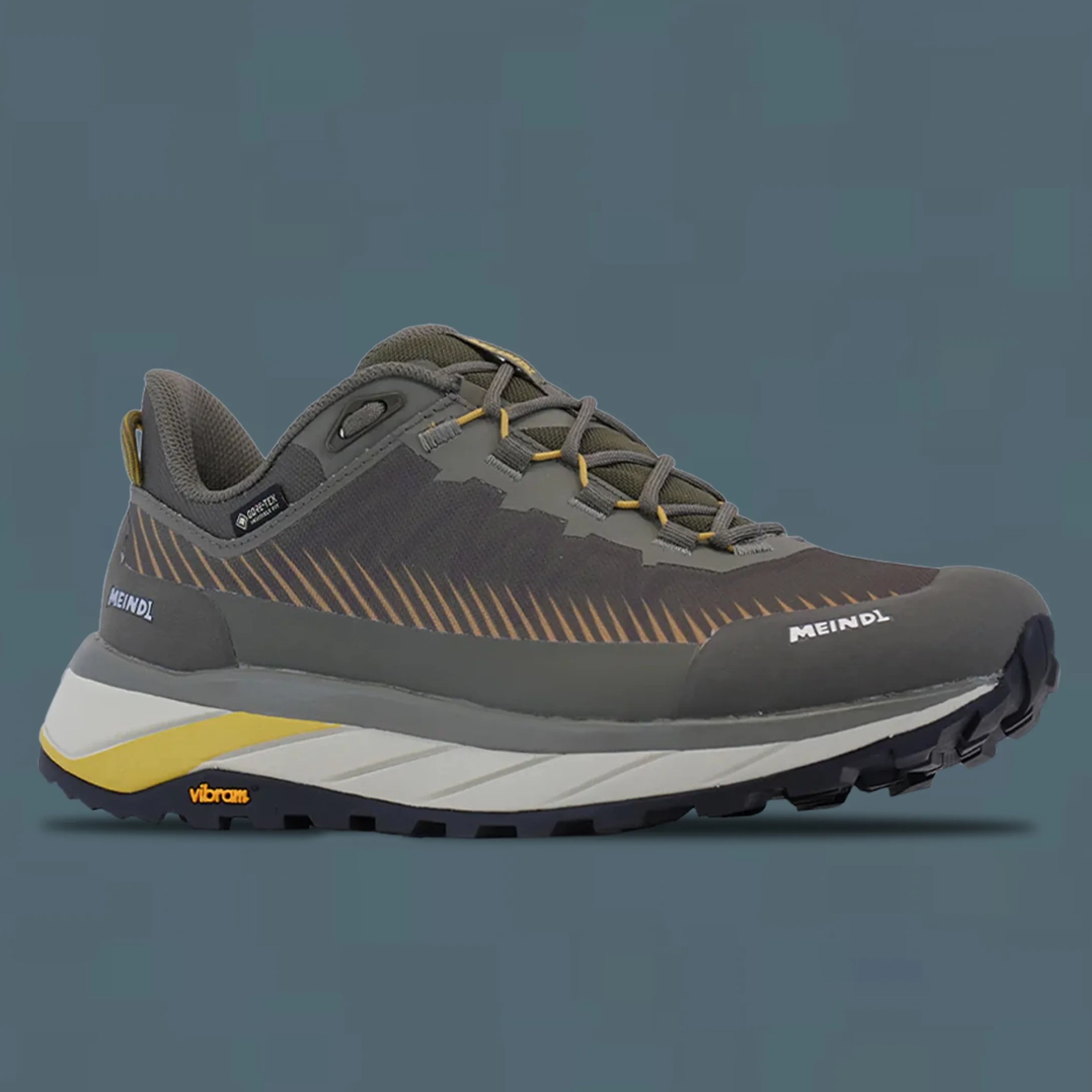 Gray and olive green Meindl hiking shoe with yellow accents and Vibram sole on a gray background.