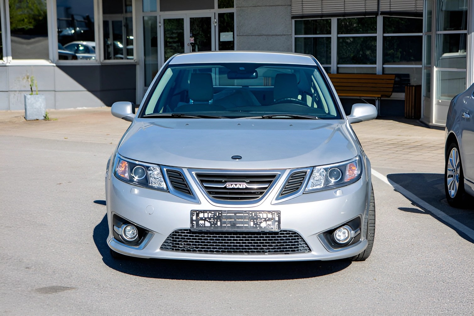 Silver Saab sedan parked in front of a building with a bench visible through the windows.