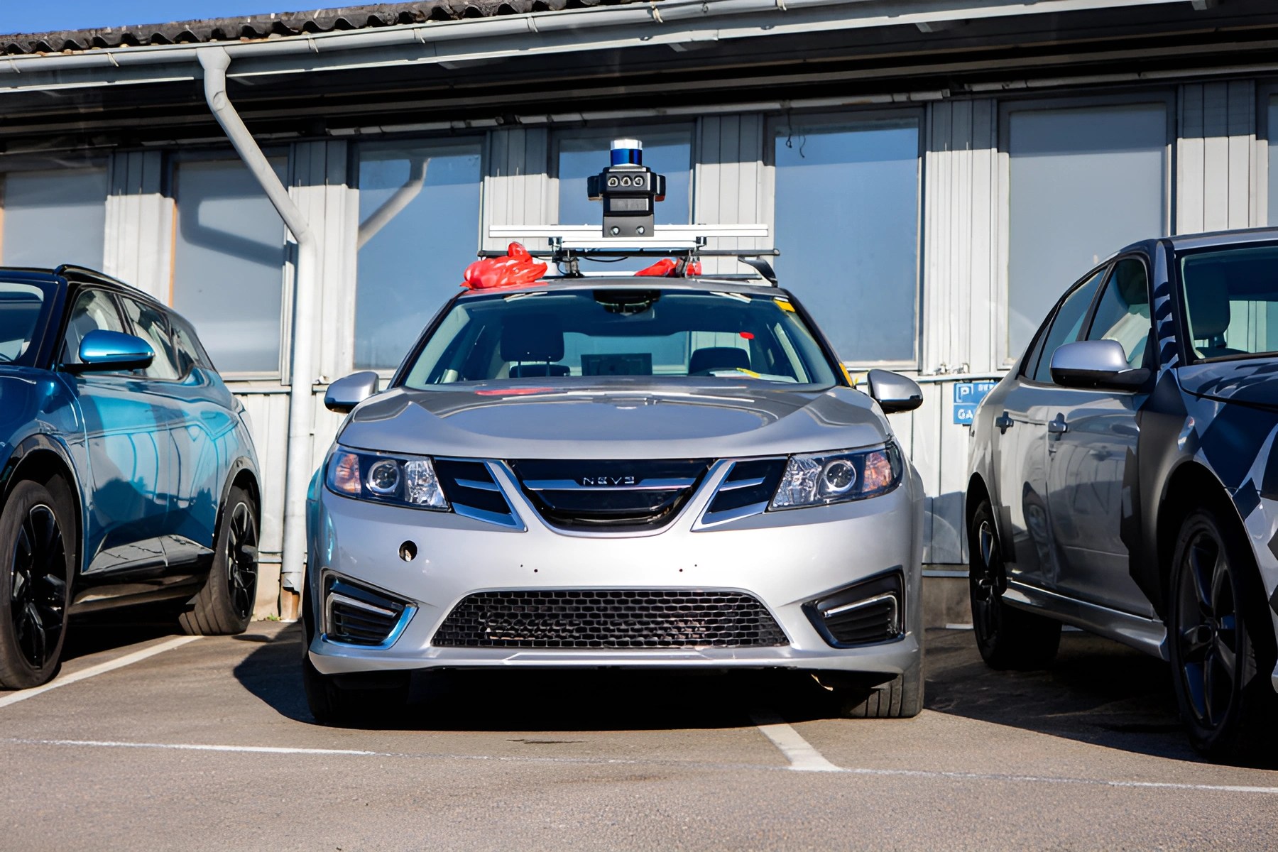Silver sedan equipped with rooftop sensors and cameras parked between two other cars.