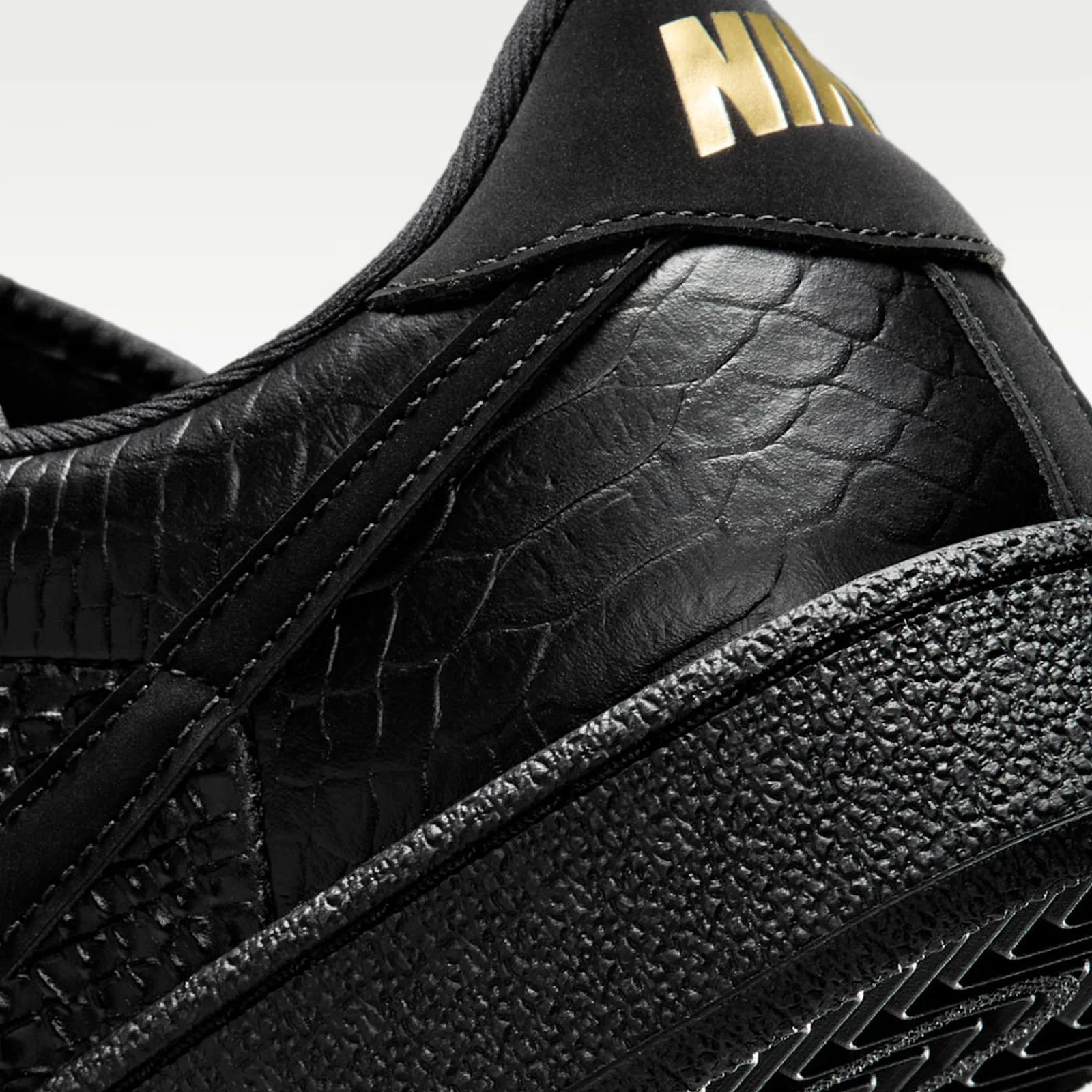 Close-up of black textured Nike sneaker with gold logo on the heel tab and detailed stitching.