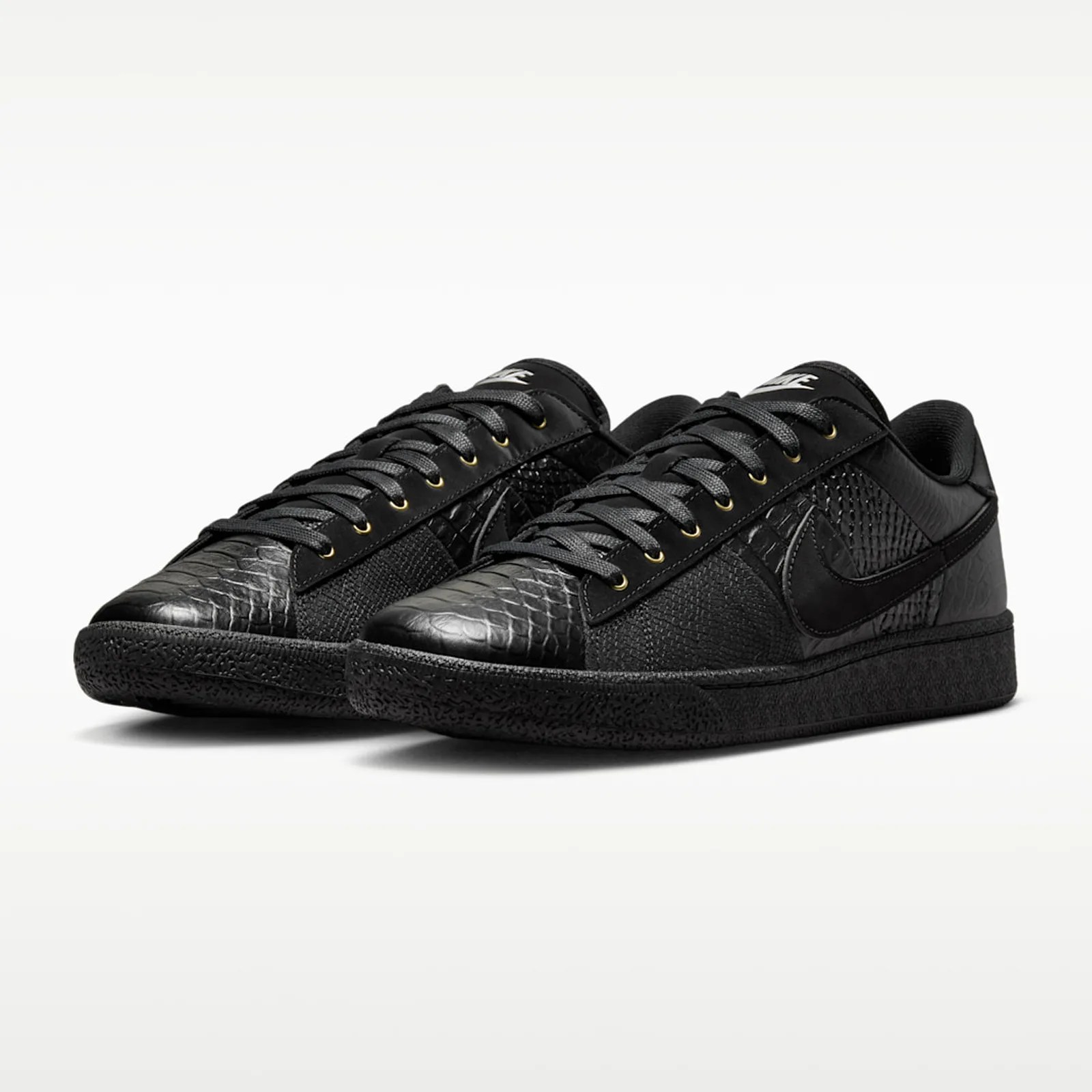 Pair of black low-top sneakers with textured snake-skin pattern and black laces on a white background.