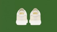 Pair of off-white Nike sneakers with gold Nike logos on the heel against a green background.