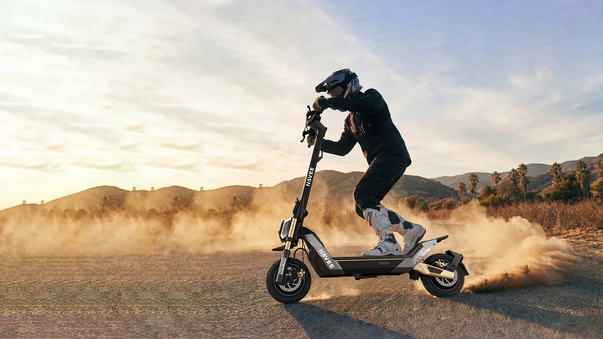 Person wearing black gear and white boots riding a black and gold Navee electric scooter on a dirt path with dust clouds.
