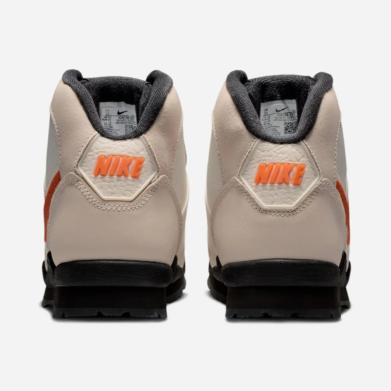 Pair of beige Nike sneakers with orange "NIKE" text on the heel and black soles, viewed from the back.