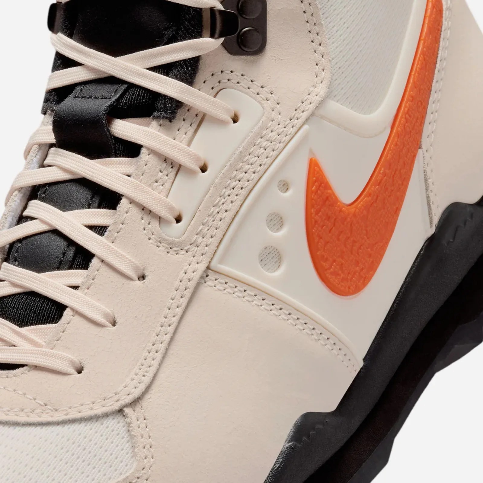 Close-up of beige and black sneaker with orange Nike swoosh and cream-colored laces.