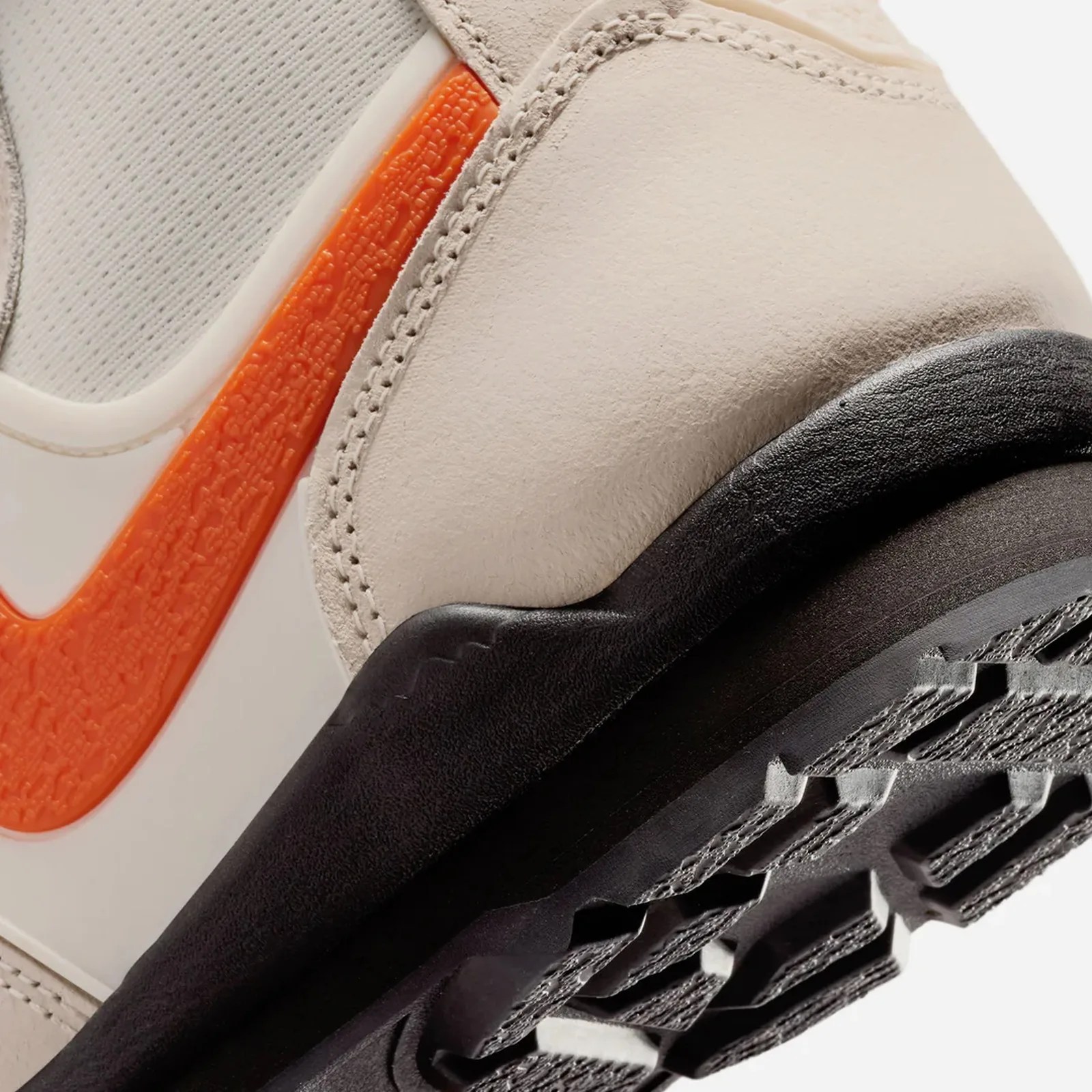 Close-up of a beige sneaker with an orange textured Nike swoosh and a black sole.