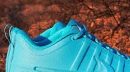 Close-up of a bright blue sneaker with textured upper and laces, set against a blurred brown outdoor background.