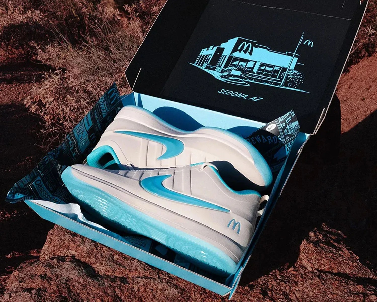 Pair of white and light blue Nike sneakers in a blue box with a McDonald's building illustration and "Sedona, AZ" text inside the lid.