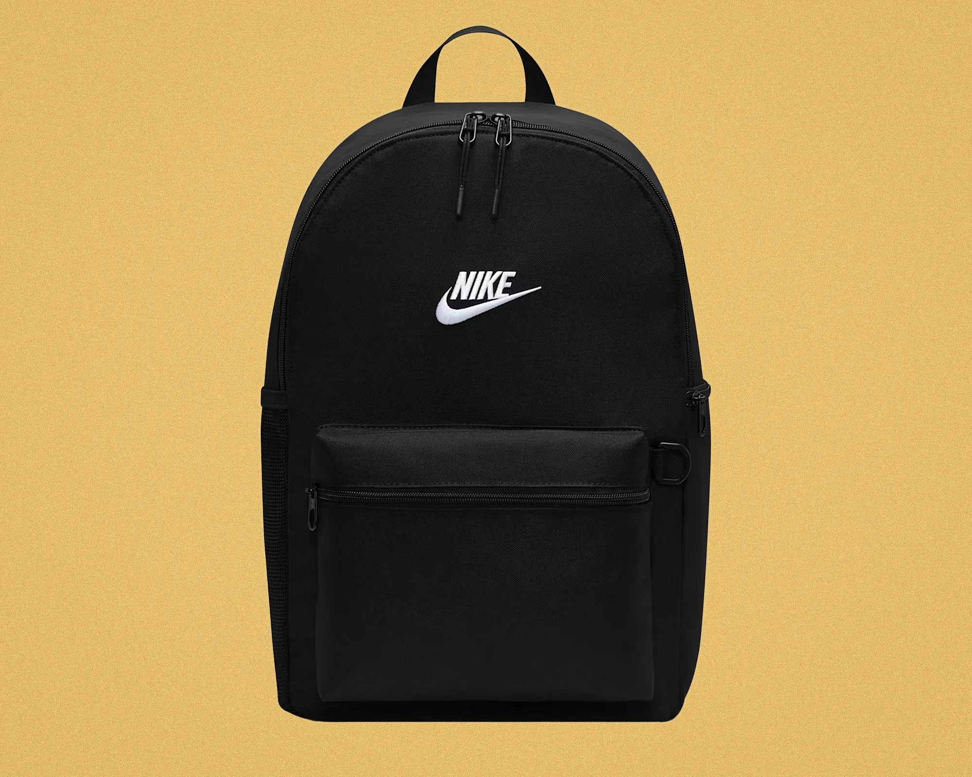 Black Nike backpack with white logo, front zippered pocket, and top handle against a beige background.