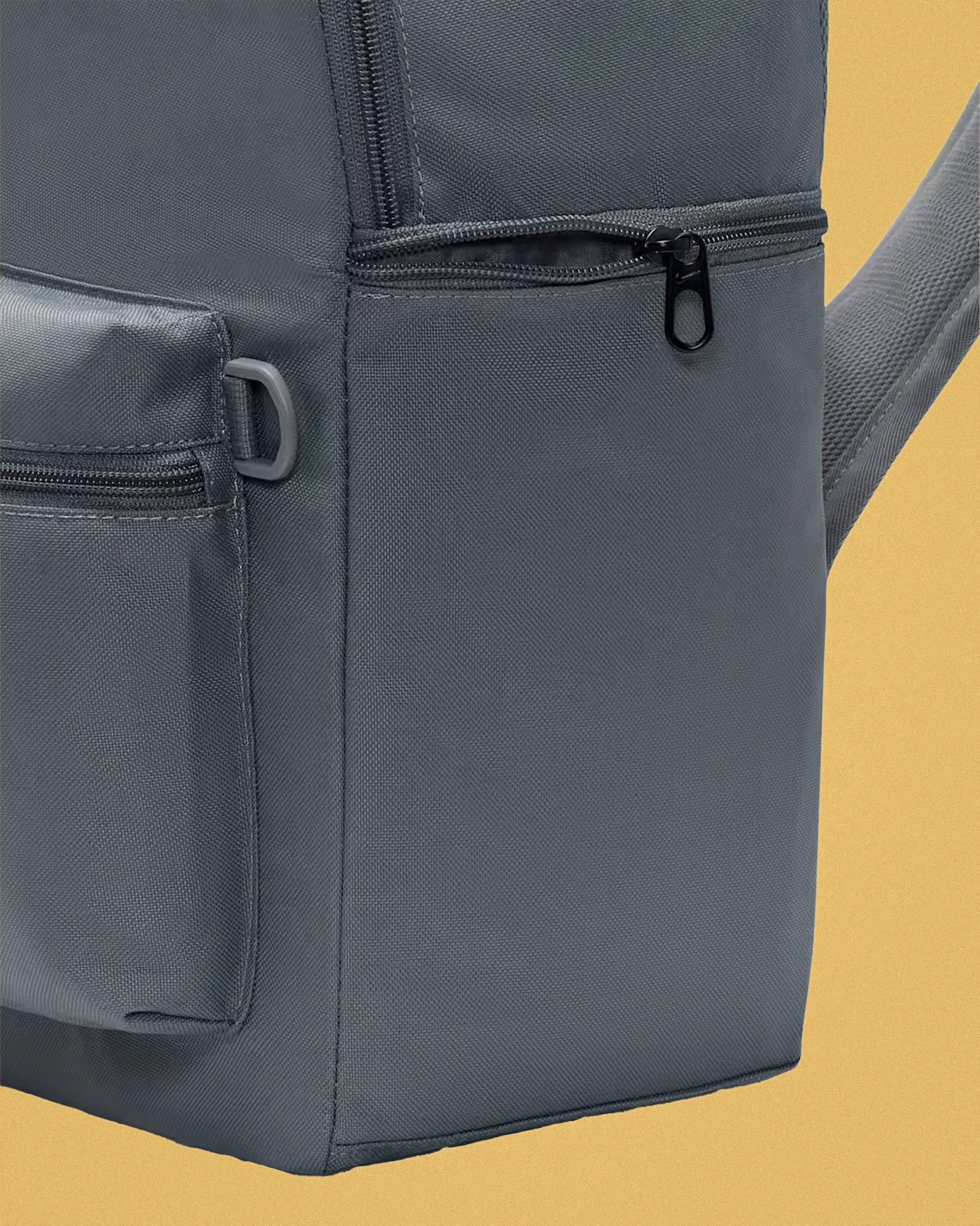 Close-up of a gray fabric backpack corner with a zipper pocket and a small plastic loop on a yellow background.