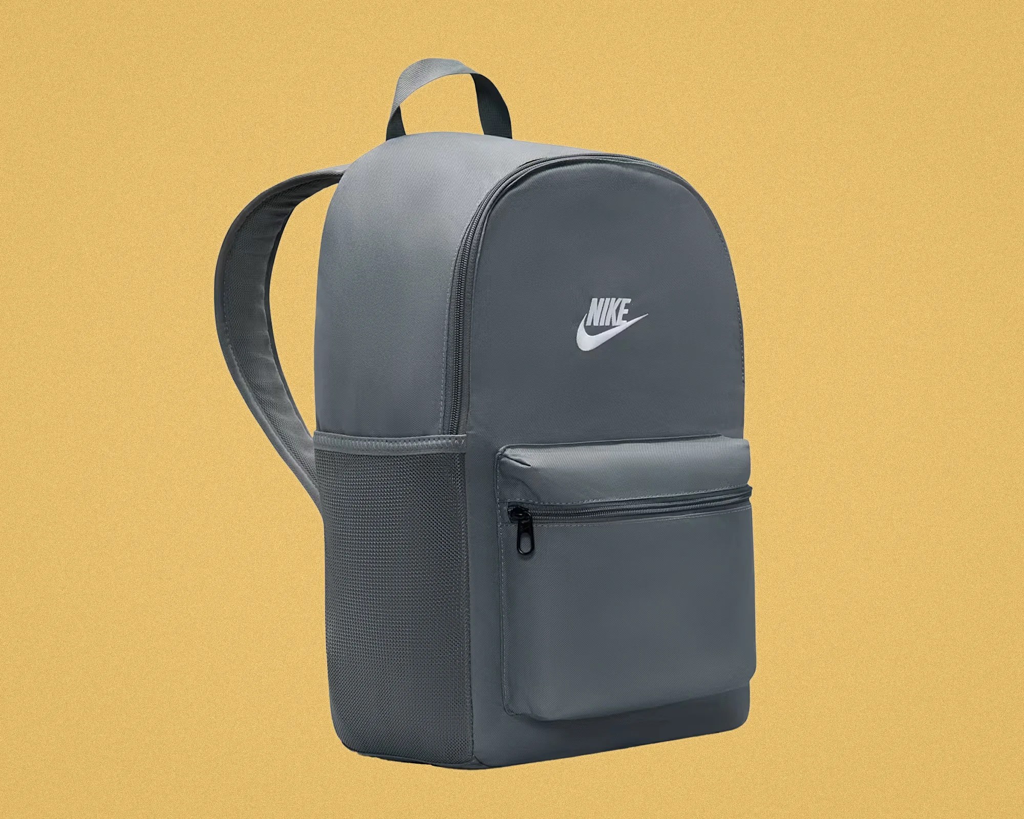 Gray Nike backpack with front zippered pocket and mesh side pocket against a yellow background.