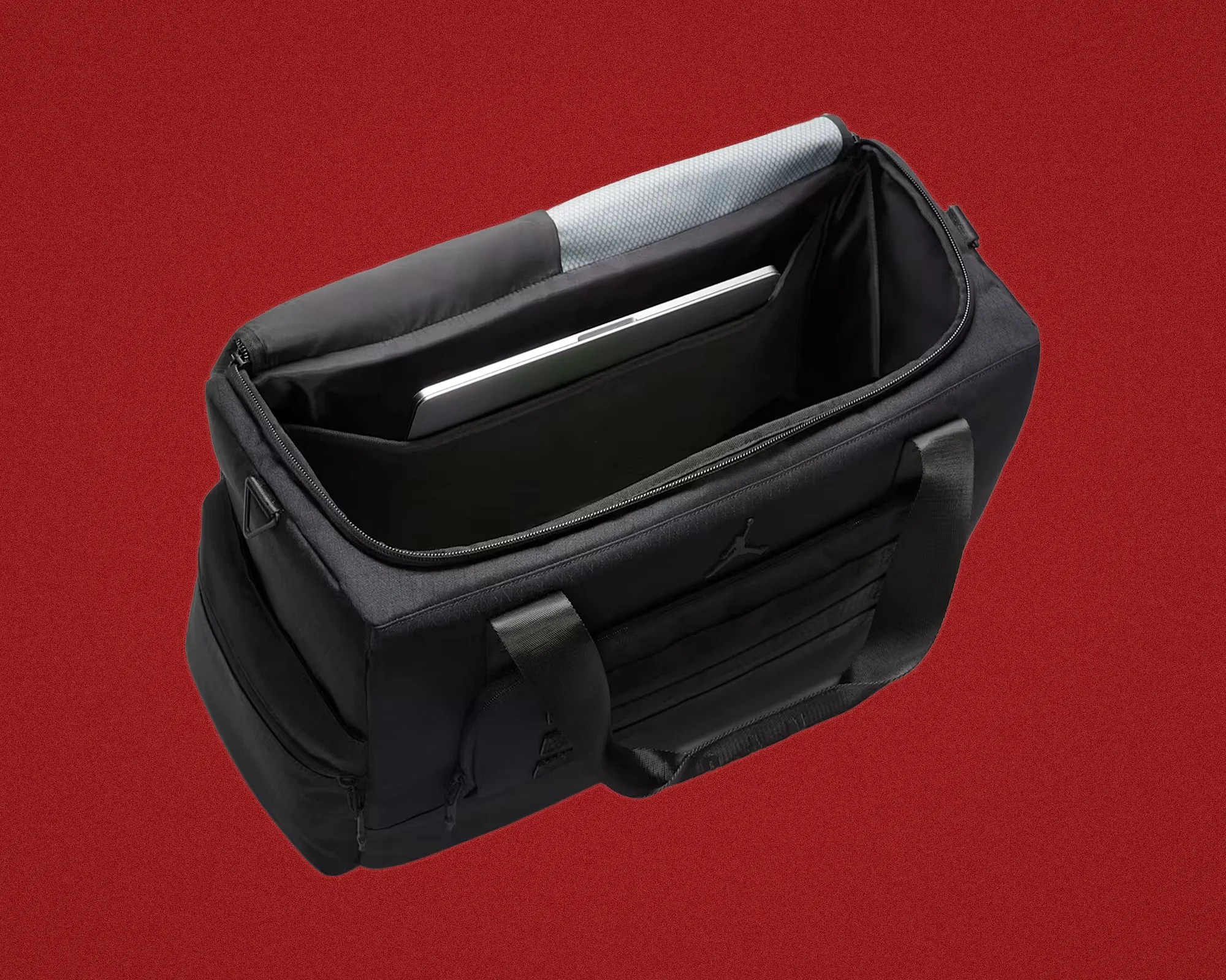 Black soft-sided bag with padded laptop compartment and gray cushioned top edge on red background.