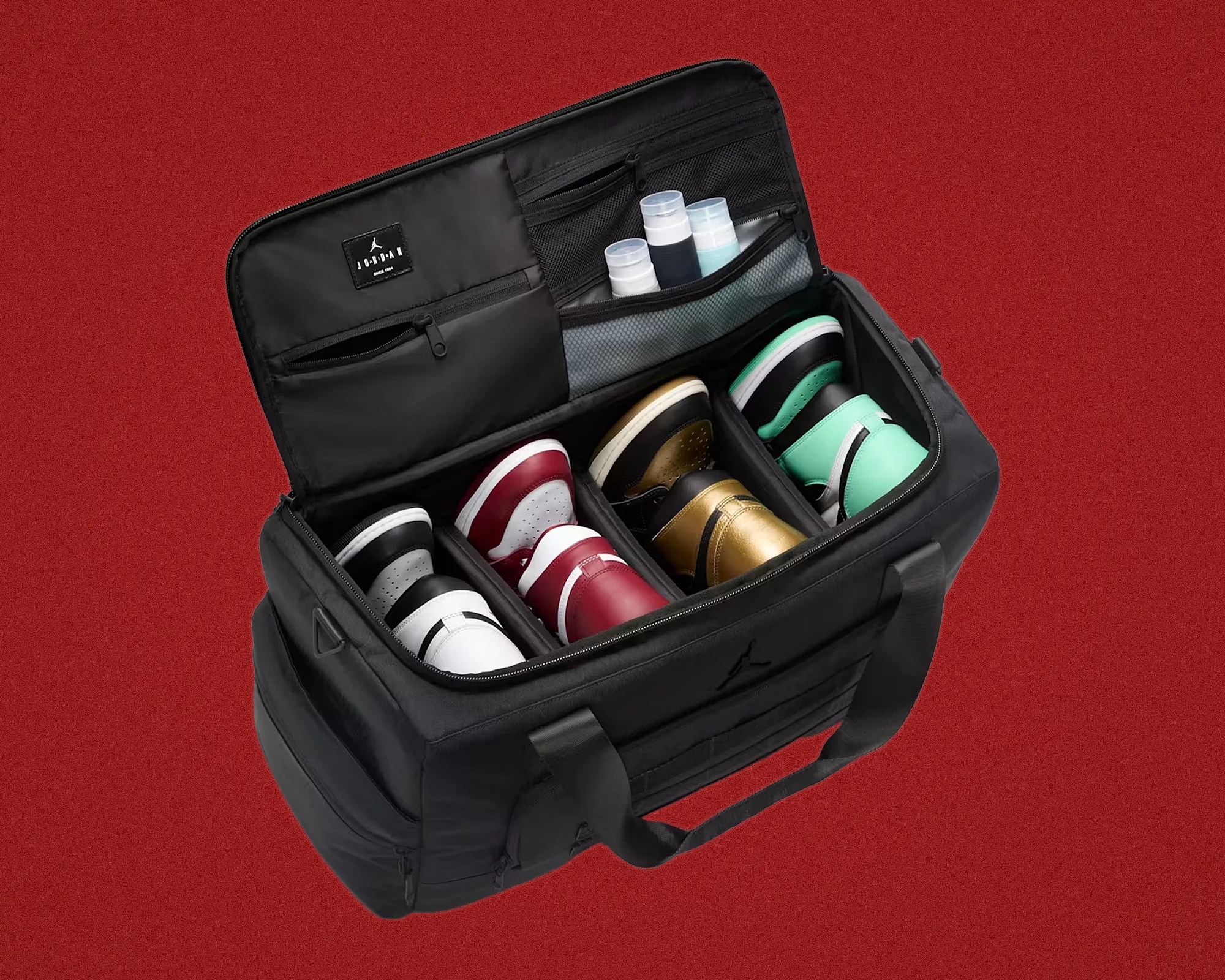 Black Jordan shoe bag with four compartments holding pairs of sneakers and three small bottles in mesh pockets.
