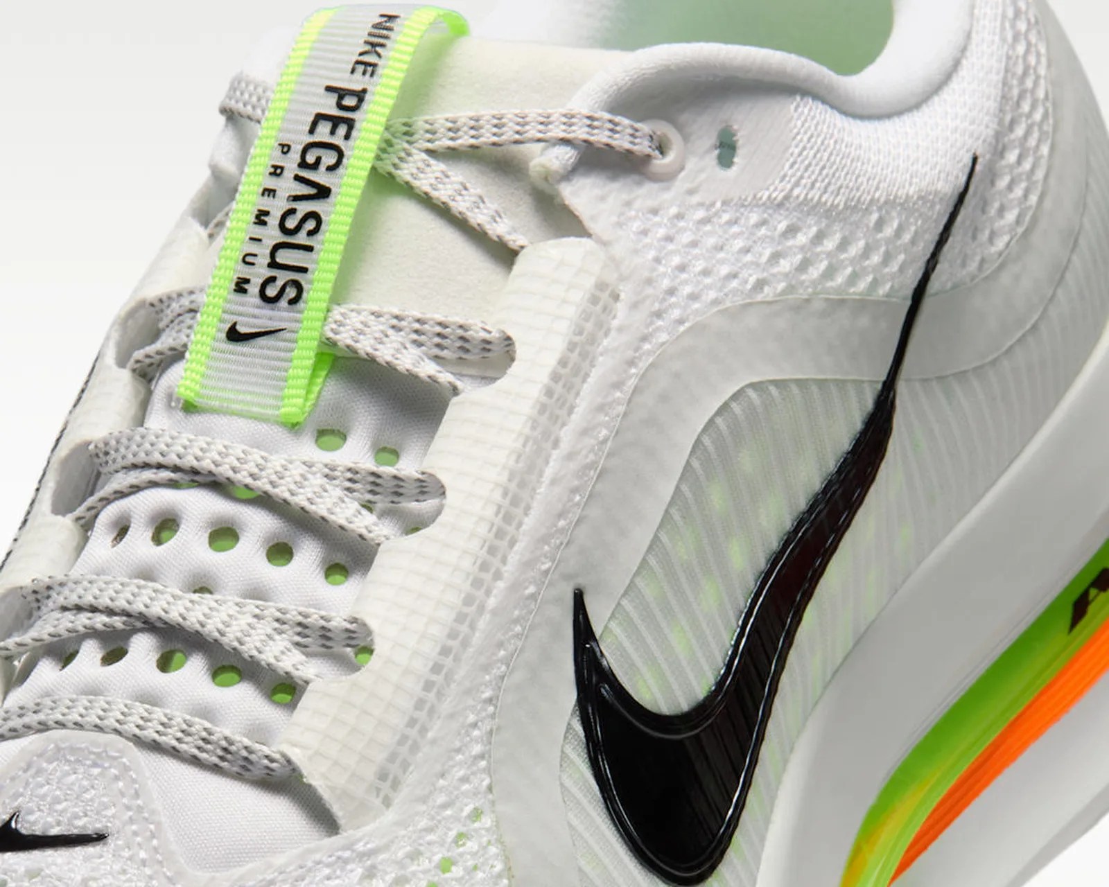 Close-up of a white Nike Pegasus Premium sneaker with gray laces, a black swoosh, and neon green and orange accents.