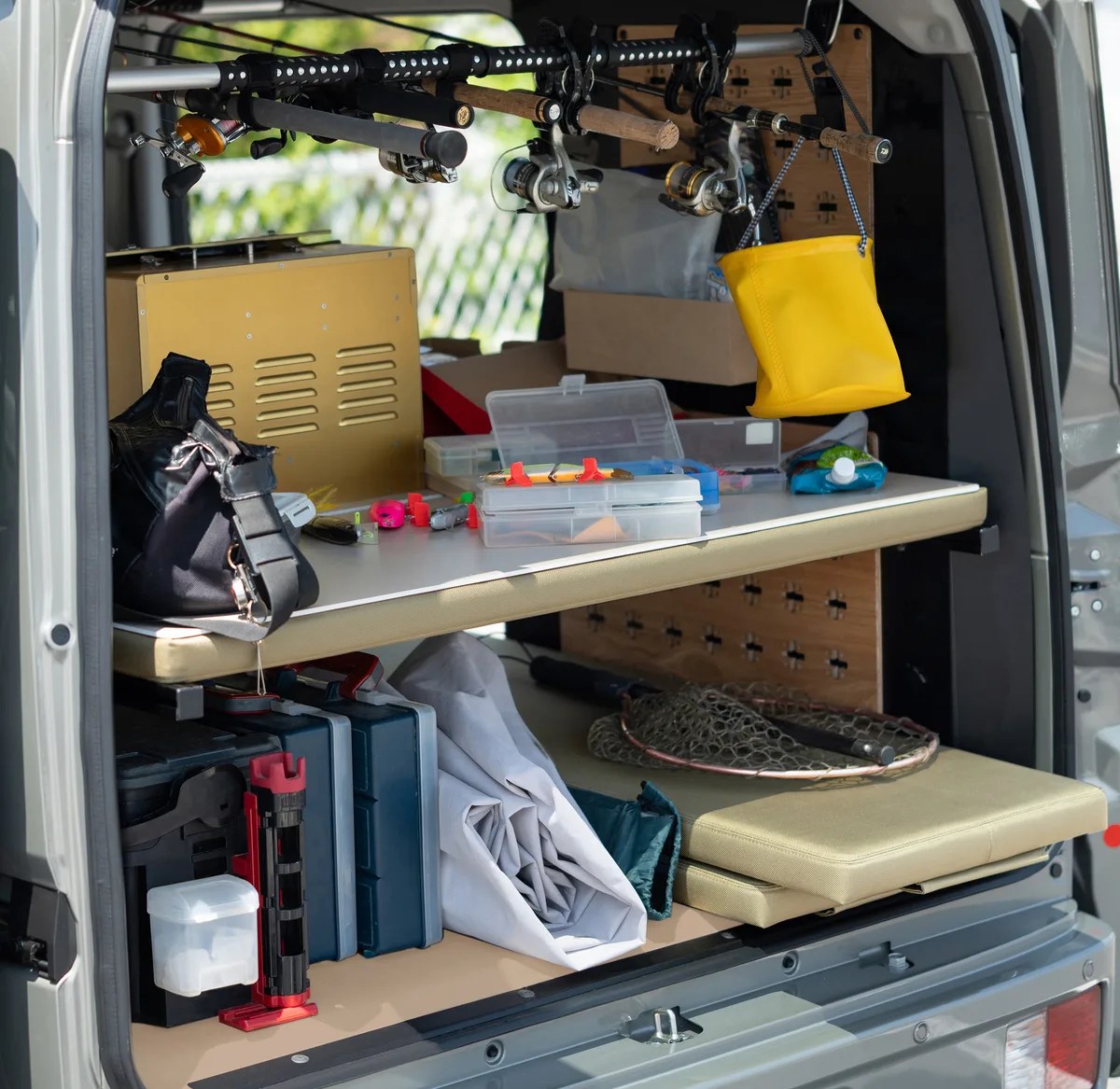 Back of a van organized with fishing rods, tackle boxes, a yellow hanging bag, and fishing nets.