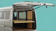 Open rear of white van showing interior with beige foldable shelf and black panel with pegboard holes.