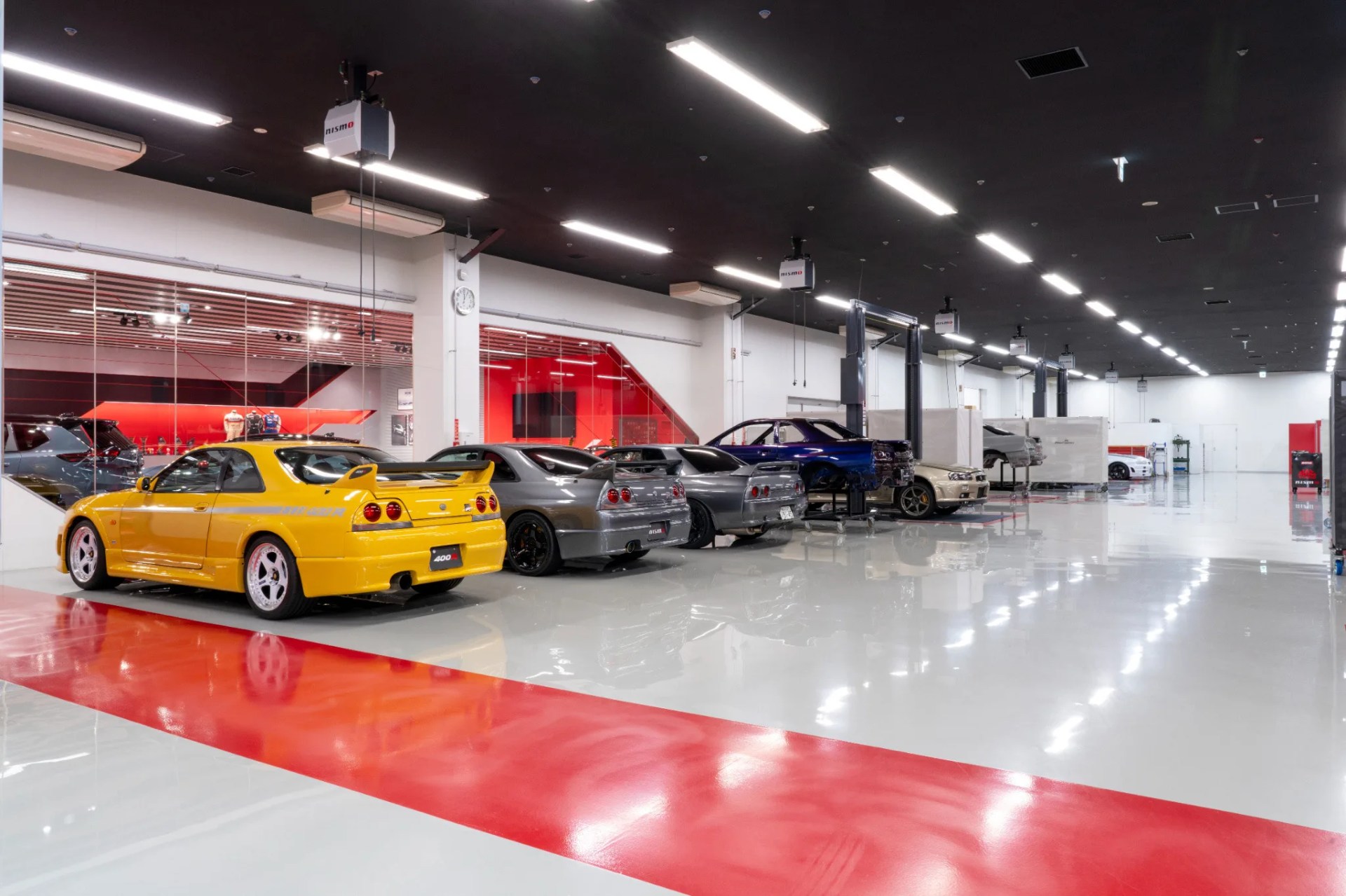 Row of Nissan Skyline sports cars in various colors inside a clean, well-lit garage with red and white flooring.