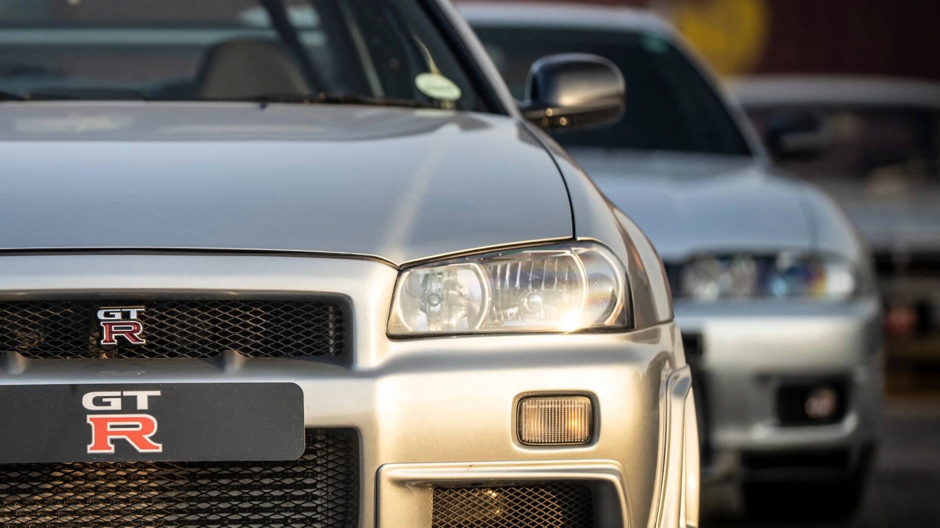 Front view of a silver Nissan GT-R car with a close-up on the headlight and grille emblem.