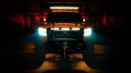 Front view of an orange Nissan truck with bright LED headlights and roof light bar in a dark garage.