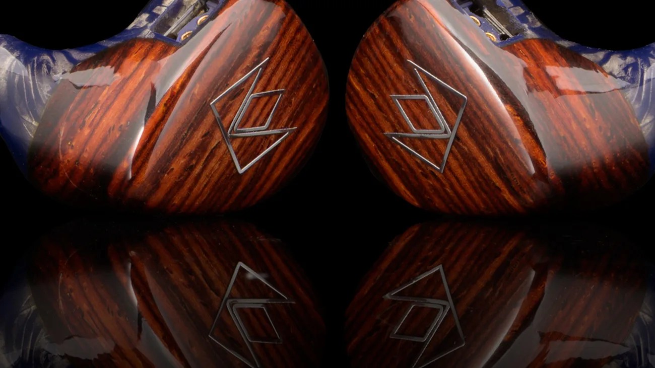 Pair of polished wooden in-ear monitors with a geometric silver logo on each face, reflecting on a black surface.