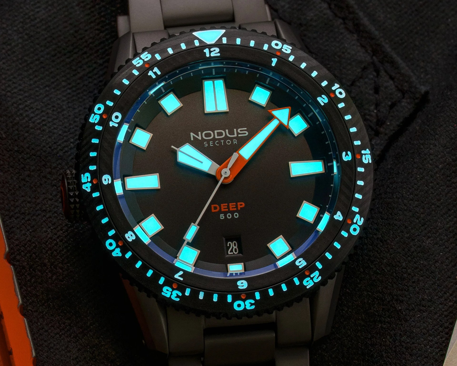 Black Nodus Sector Deep 500 dive watch with glowing blue hour markers and hands on a black fabric surface.