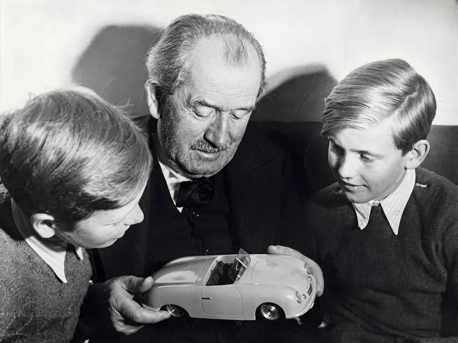 Older man and two boys closely examining a model of a vintage convertible car.