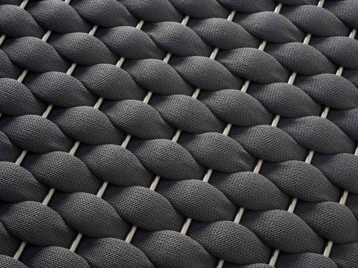 Close-up of dark gray knitted fabric loops interwoven with thin metal rods in a repeating pattern.