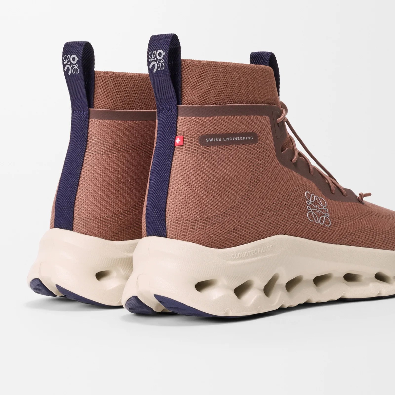 Brown high-top sneakers with navy pull tabs, white Swiss flag tag, and cream-colored soles with cutout details.