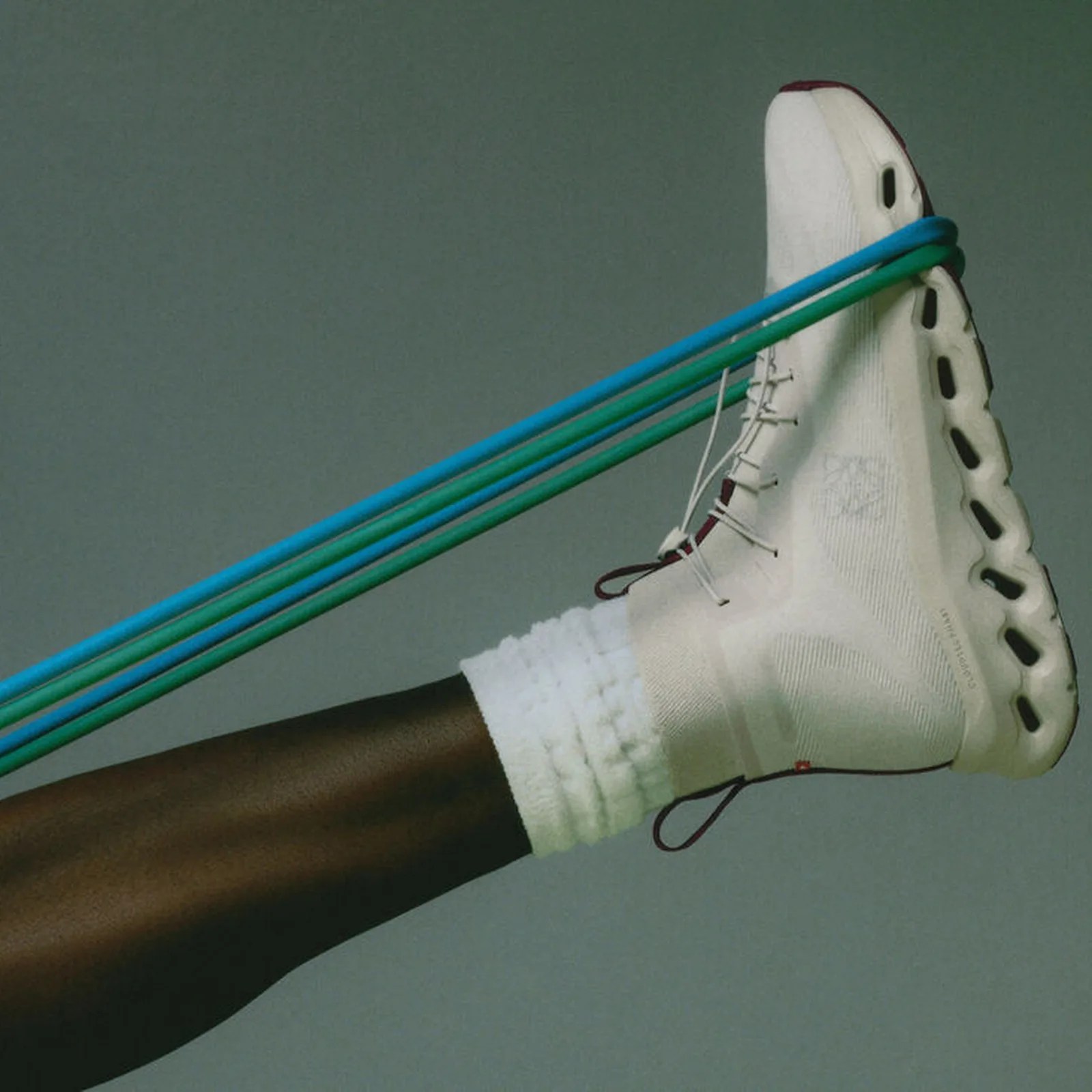 White high-top athletic shoe with black sole and maroon accents, worn with white socks and resistance bands around the foot.