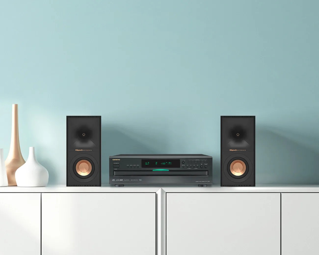 Black Onkyo stereo receiver with digital display and two black Klipsch speakers with copper cones on a white cabinet.