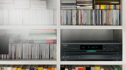Black Onkyo DX-C390 compact disc changer with digital display on a white shelf surrounded by CDs and books.