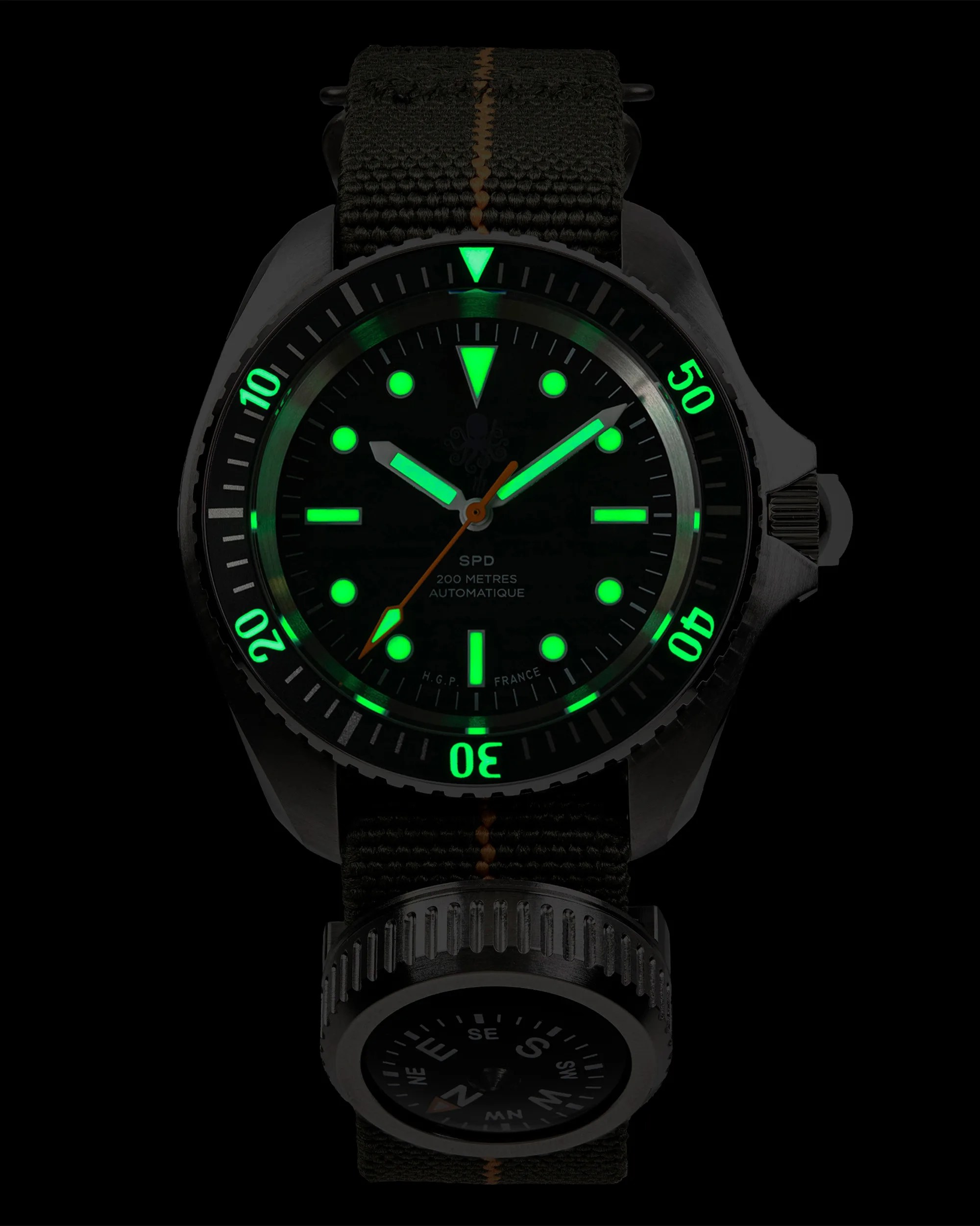 Diver watch with glowing green markers and hands, black fabric strap with orange stitching, and attached compass.