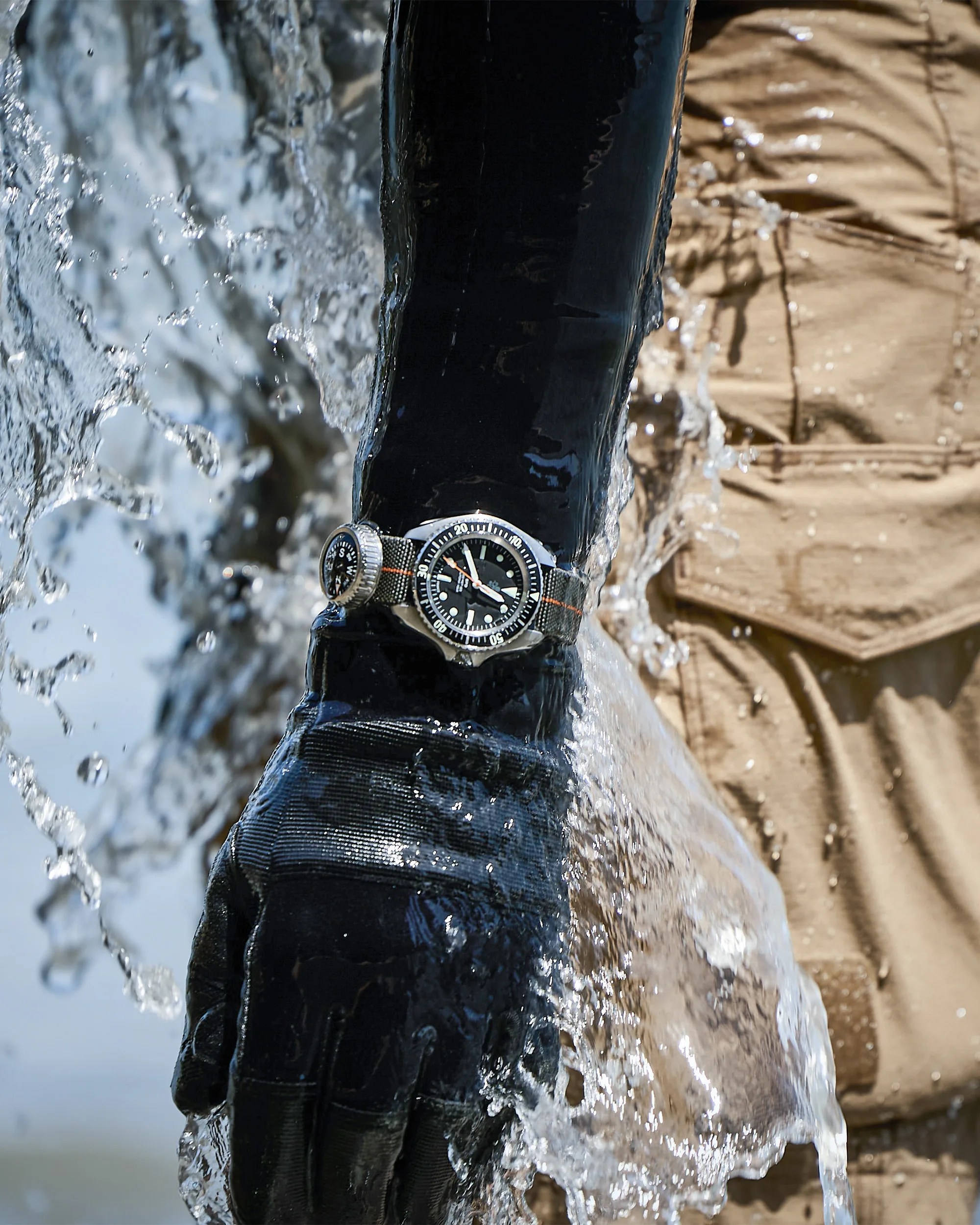 Black diving glove with a wristwatch and compass strap, splashed with water.