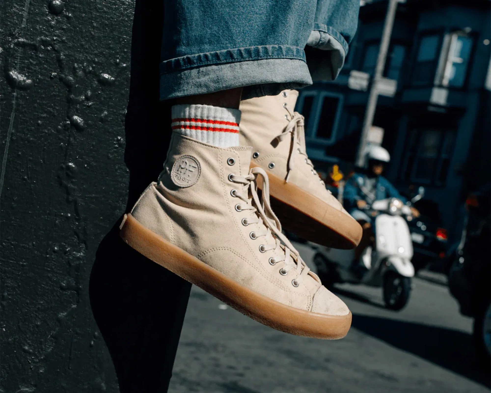 Beige high-top canvas sneakers with gum soles and white socks with red stripes, worn with cuffed blue jeans.