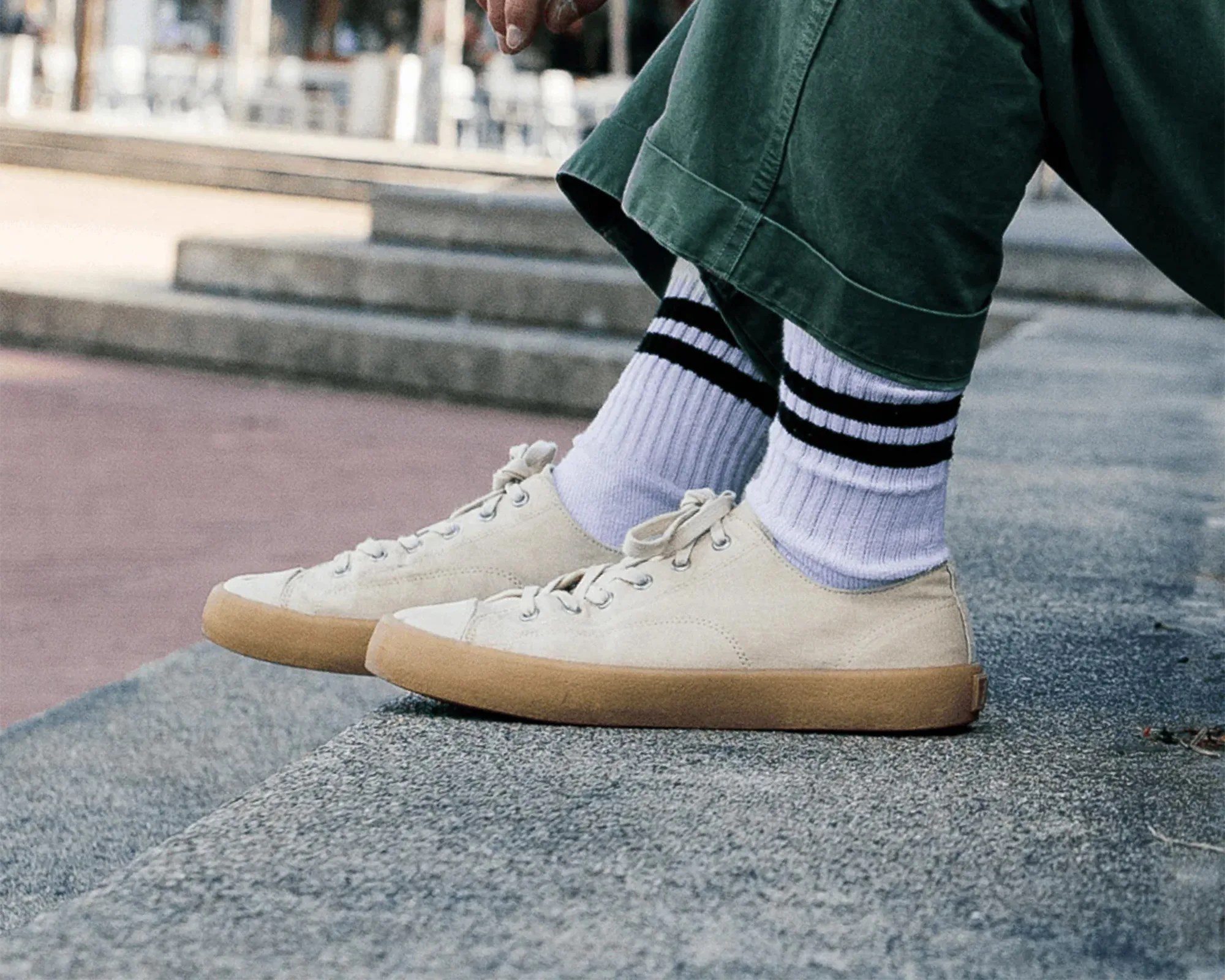 Off-white canvas sneakers with gum soles worn with white socks featuring two black stripes and green pants.